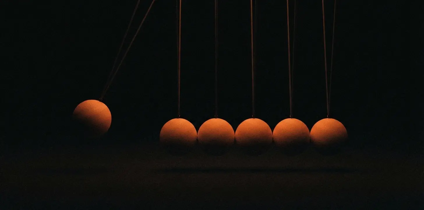 A Newton's cradle mid-swing, one amber ball lifted away from the row, against near-black